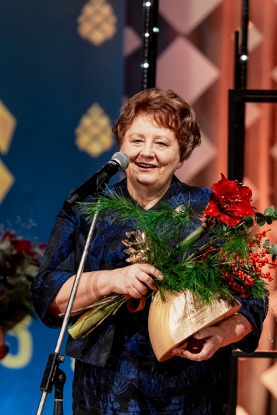 Sieviete ar balvu un ziediem rokās runā pie mikrofona