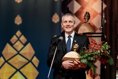 Vīrietis ar ziediem un balvu rokās runā mikrofonā